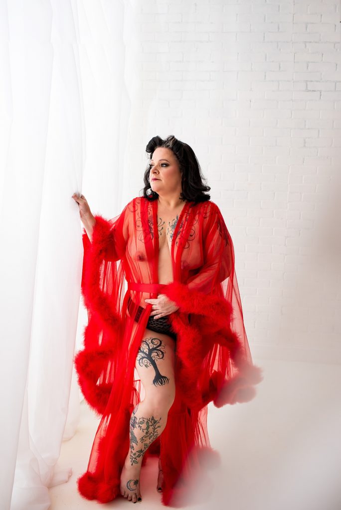 tattooed woman posing in red robe for pin up boudoir photo session