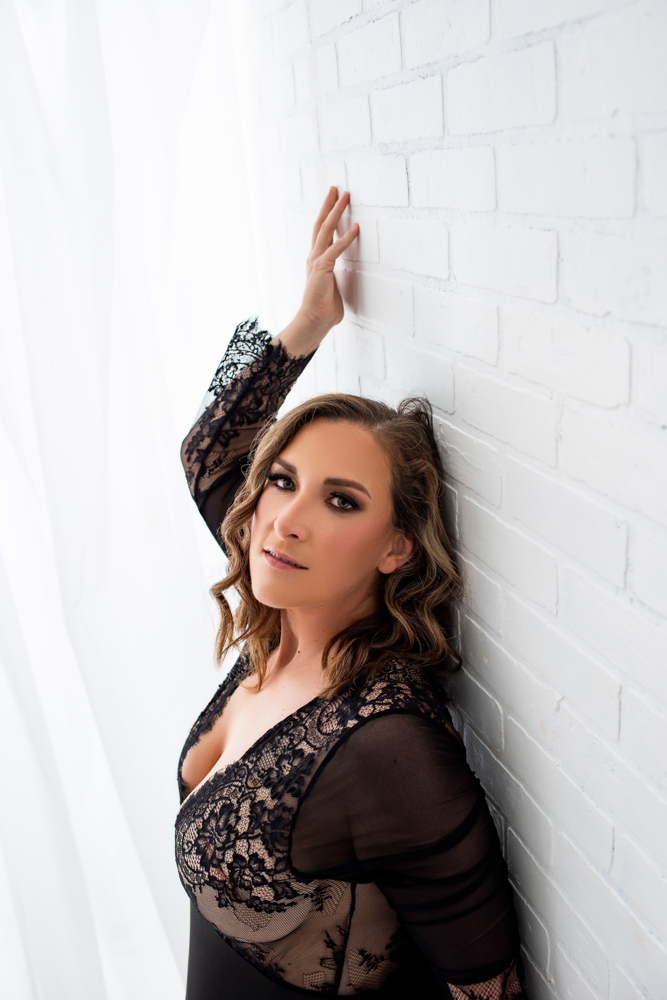 woman filled with self love while leaning up against white wall wearing black outfit