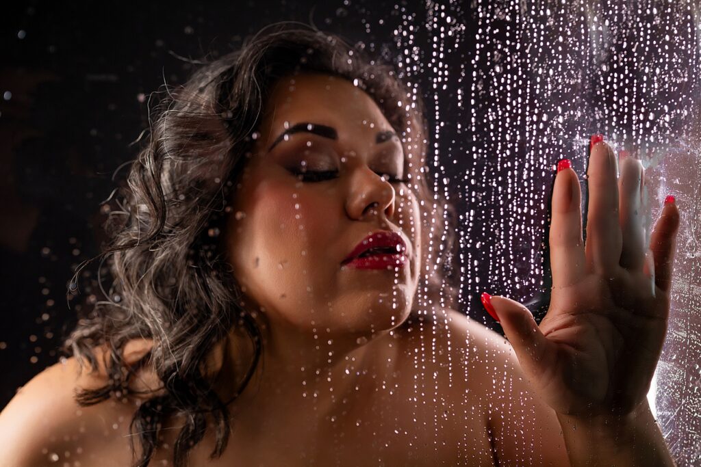 Woman sitting in chair in middle of boudoir studio having makeup applied to her face before her boudoir portrait expereince